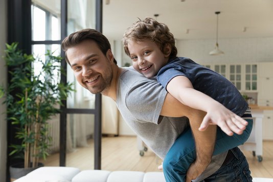 Haus-Familie-Wohnen-Serie-3-20 Vater mit Sohn auf dem Rücken im Wohnzimmer